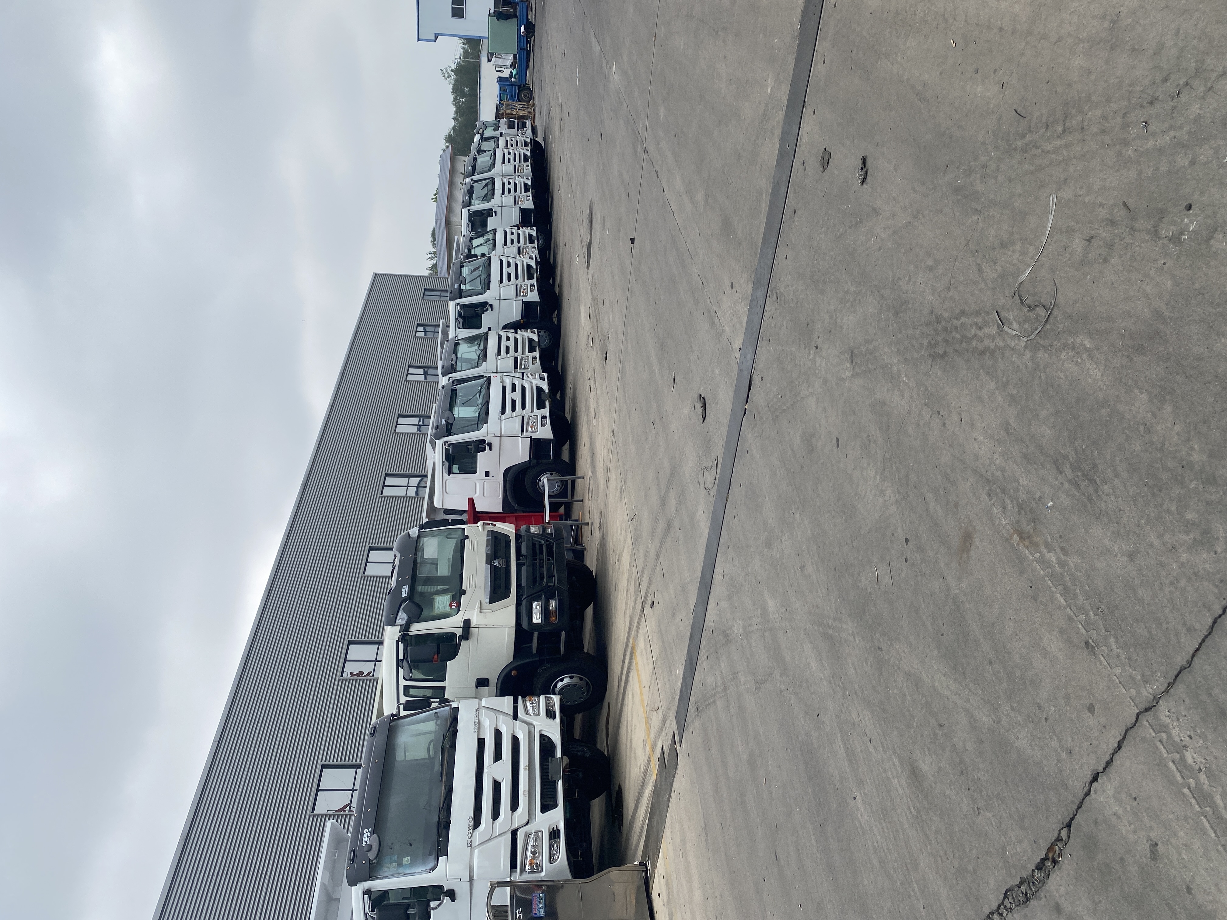 Used heavy trucks parked in a row outside a workshop building at a dealer yard in Liangshan, China